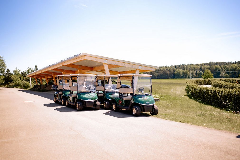 Mehrere Golfcarts vor einem Golfplatz.