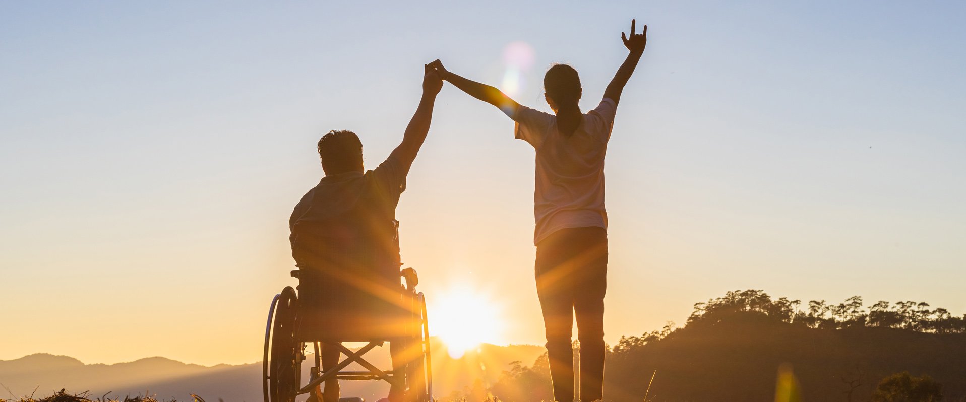 Zwei Personen vor Sonnenuntergang, eine Person sitzt im Rollstuhl